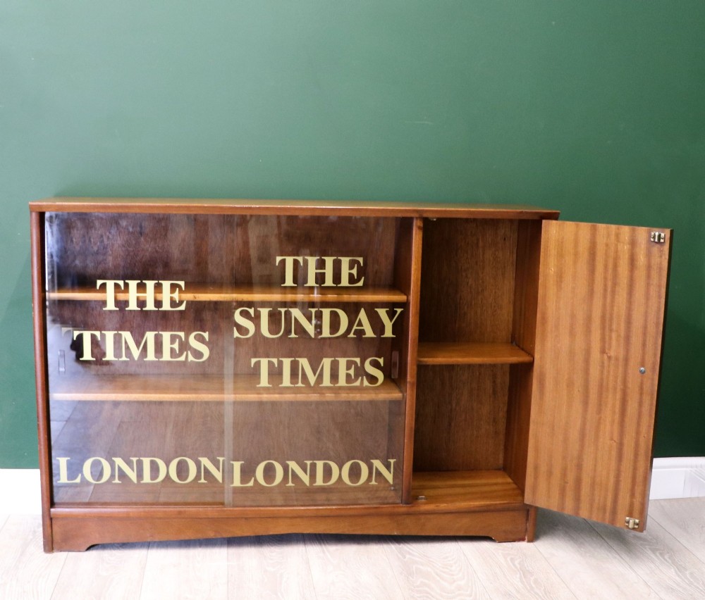 A low mid-century teak bookcase with two sliding glass doors featuring printed lettering alongside a single solid teak cupboard door. View IV