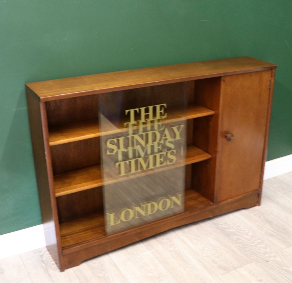 A low mid-century teak bookcase with two sliding glass doors featuring printed lettering alongside a single solid teak cupboard door. View VI