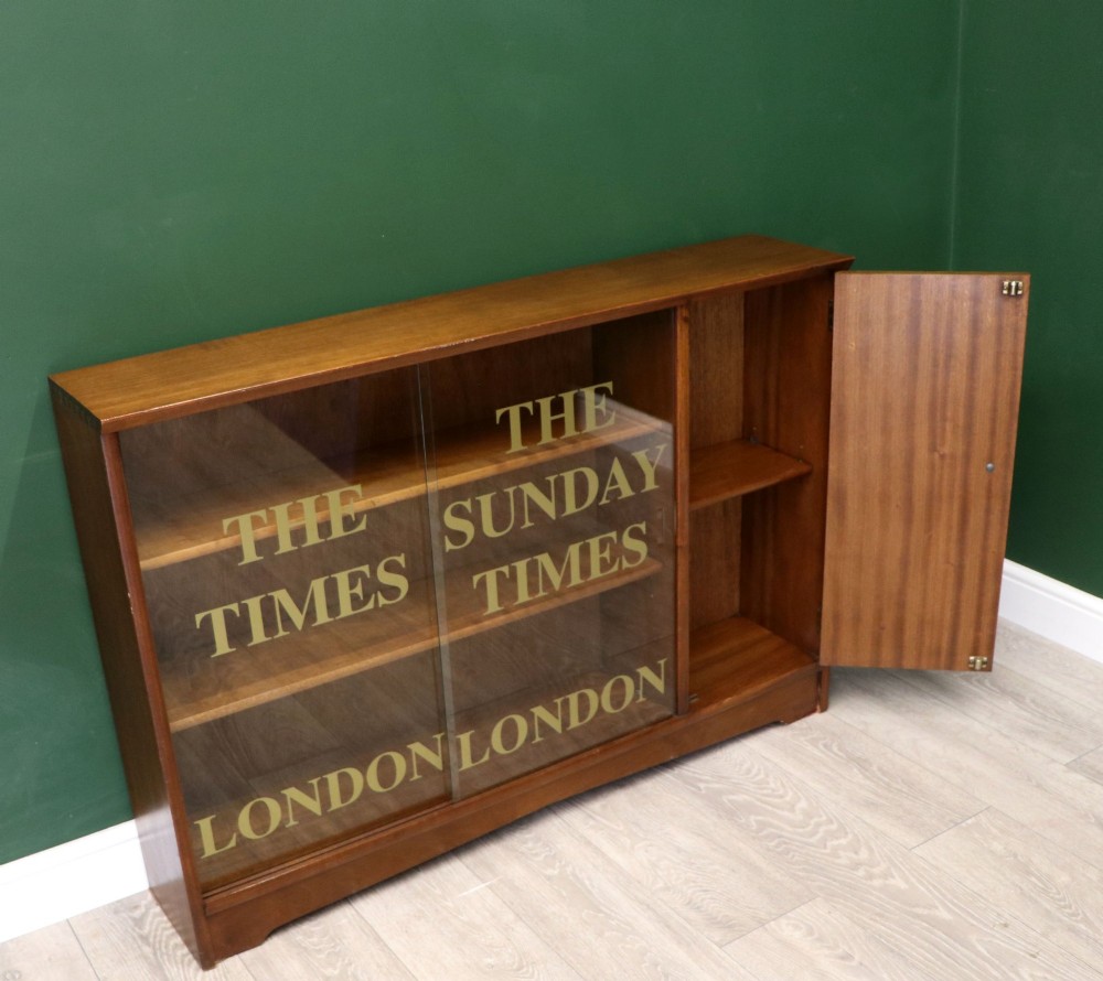 A low mid-century teak bookcase with two sliding glass doors featuring printed lettering alongside a single solid teak cupboard door. View VII