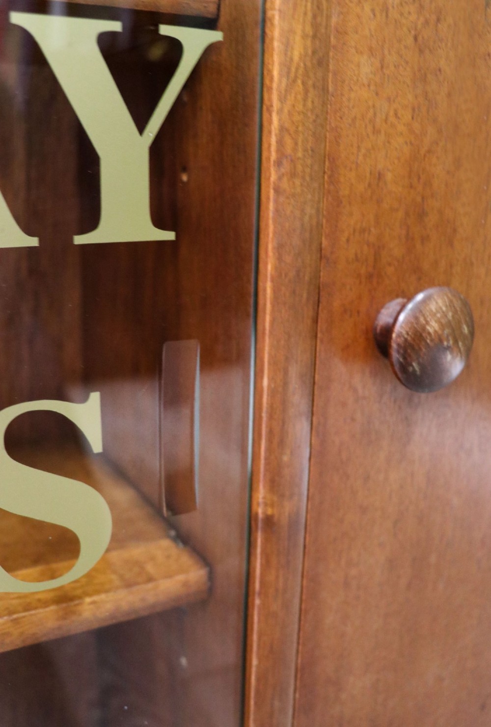 A low mid-century teak bookcase with two sliding glass doors featuring printed lettering alongside a single solid teak cupboard door. View IX