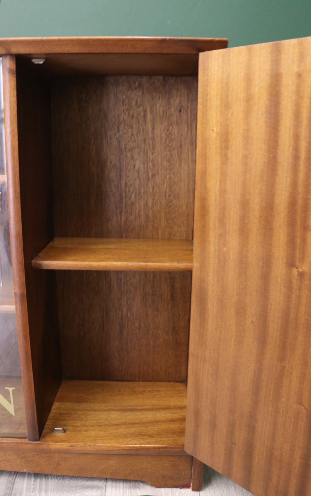 A low mid-century teak bookcase with two sliding glass doors featuring printed lettering alongside a single solid teak cupboard door. View X