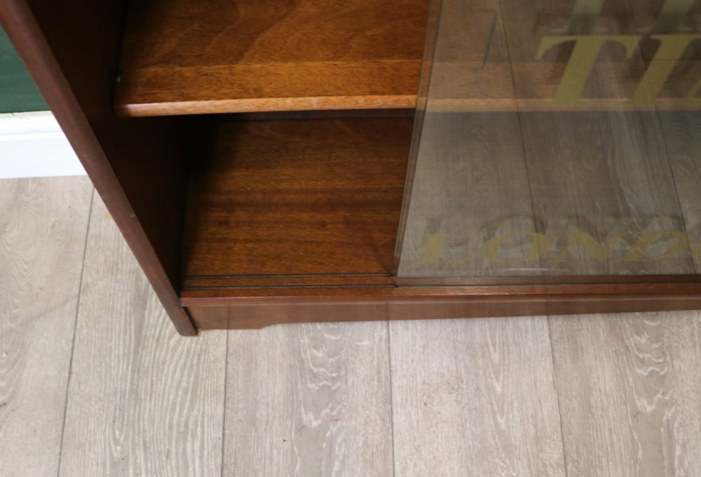 A low mid-century teak bookcase with two sliding glass doors featuring printed lettering alongside a single solid teak cupboard door. View XV