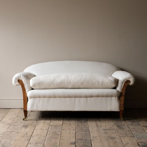 fig 1. An early 20th-century deep-seated two-seater sofa upholstered in cream calico fabric with exposed wooden side framework and brass castors.