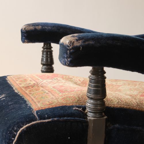 fig 1. A 19th-century open armchair featuring dark navy blue velvet upholstery combined with an oriental carpet panel across the backrest and seat, resting on turned front legs with castors.