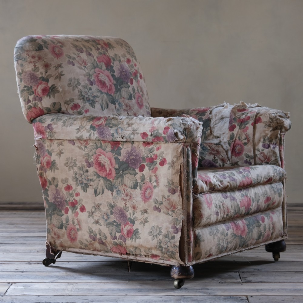 An early 20th-century upholstered armchair featuring floral chintz fabric, a deep seat cushion, turned wooden front legs, and brass castors.