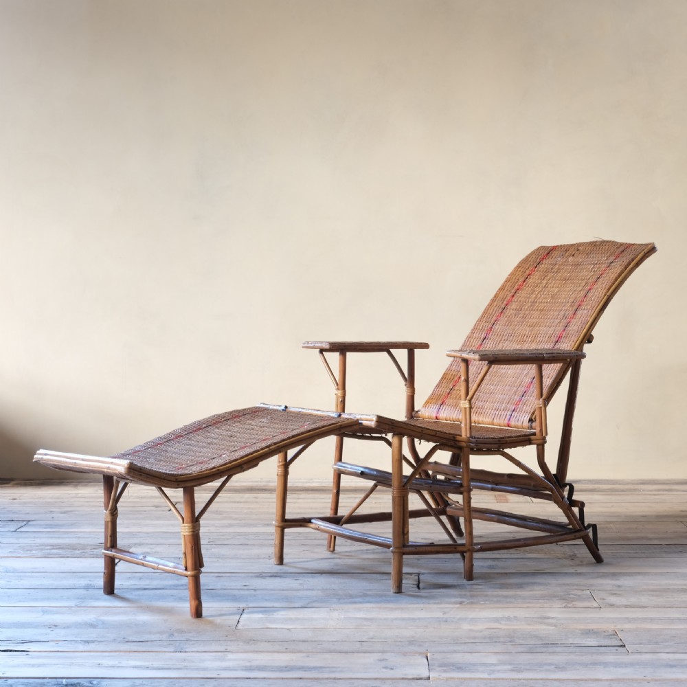 An antique French bamboo reclining chaise longue with a woven cane seat, raised armrests, and extending footrest.