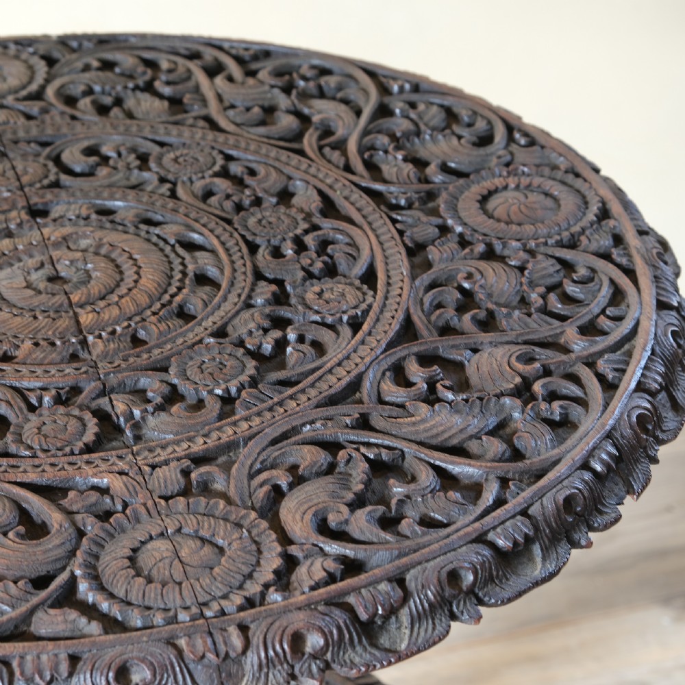 A late 19th-century Burmese dark teak two-tier side table with hand-carved mythological figure supports and circular foliate-carved surfaces. View III