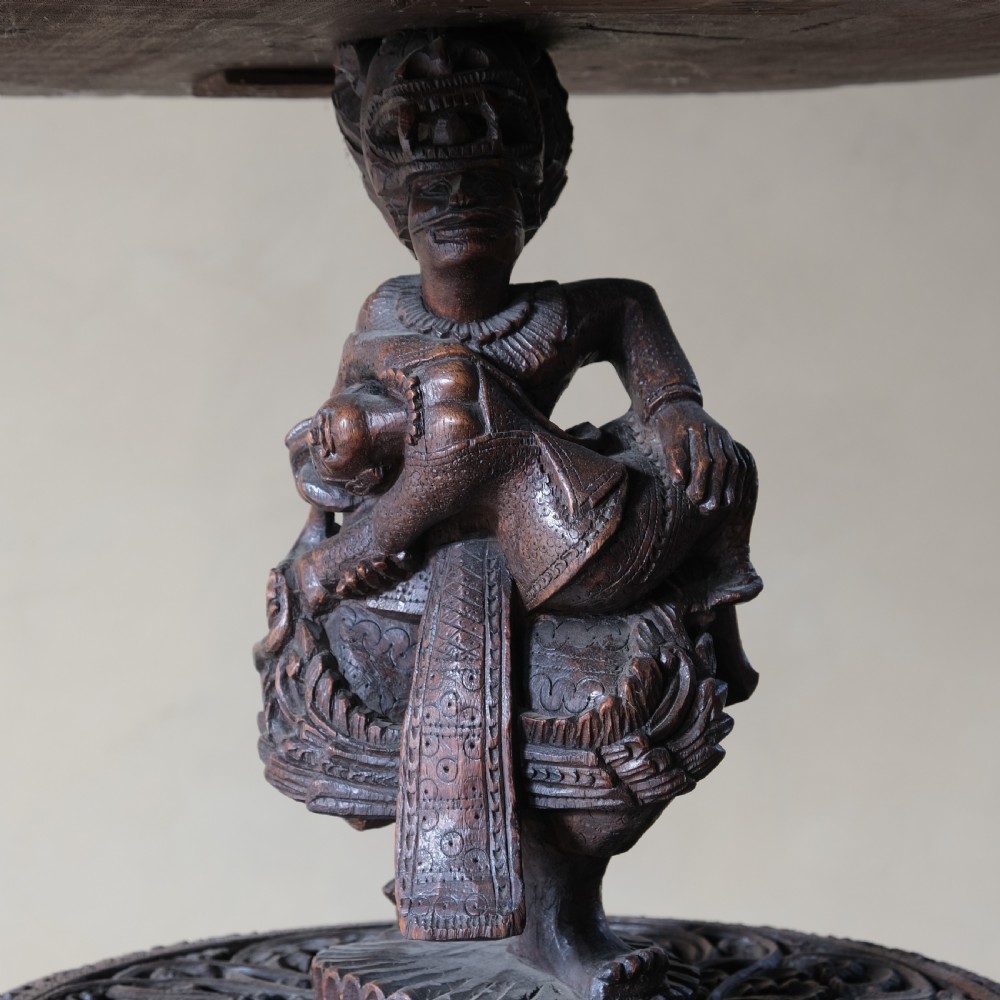 A late 19th-century Burmese dark teak two-tier side table with hand-carved mythological figure supports and circular foliate-carved surfaces. View IX