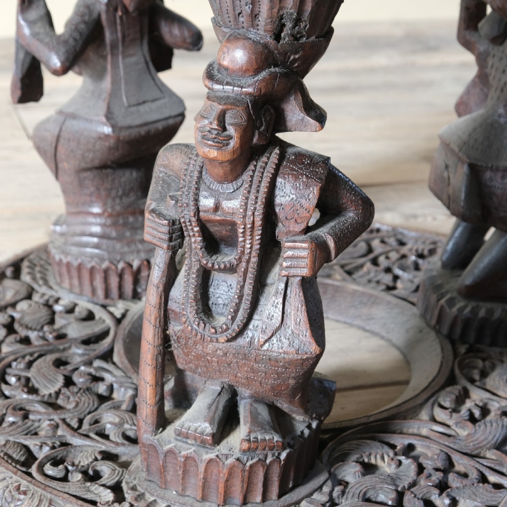 A late 19th-century Burmese dark teak two-tier side table with hand-carved mythological figure supports and circular foliate-carved surfaces. View XI
