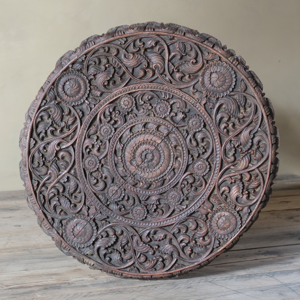 A late 19th-century Burmese dark teak two-tier side table with hand-carved mythological figure supports and circular foliate-carved surfaces. View XII