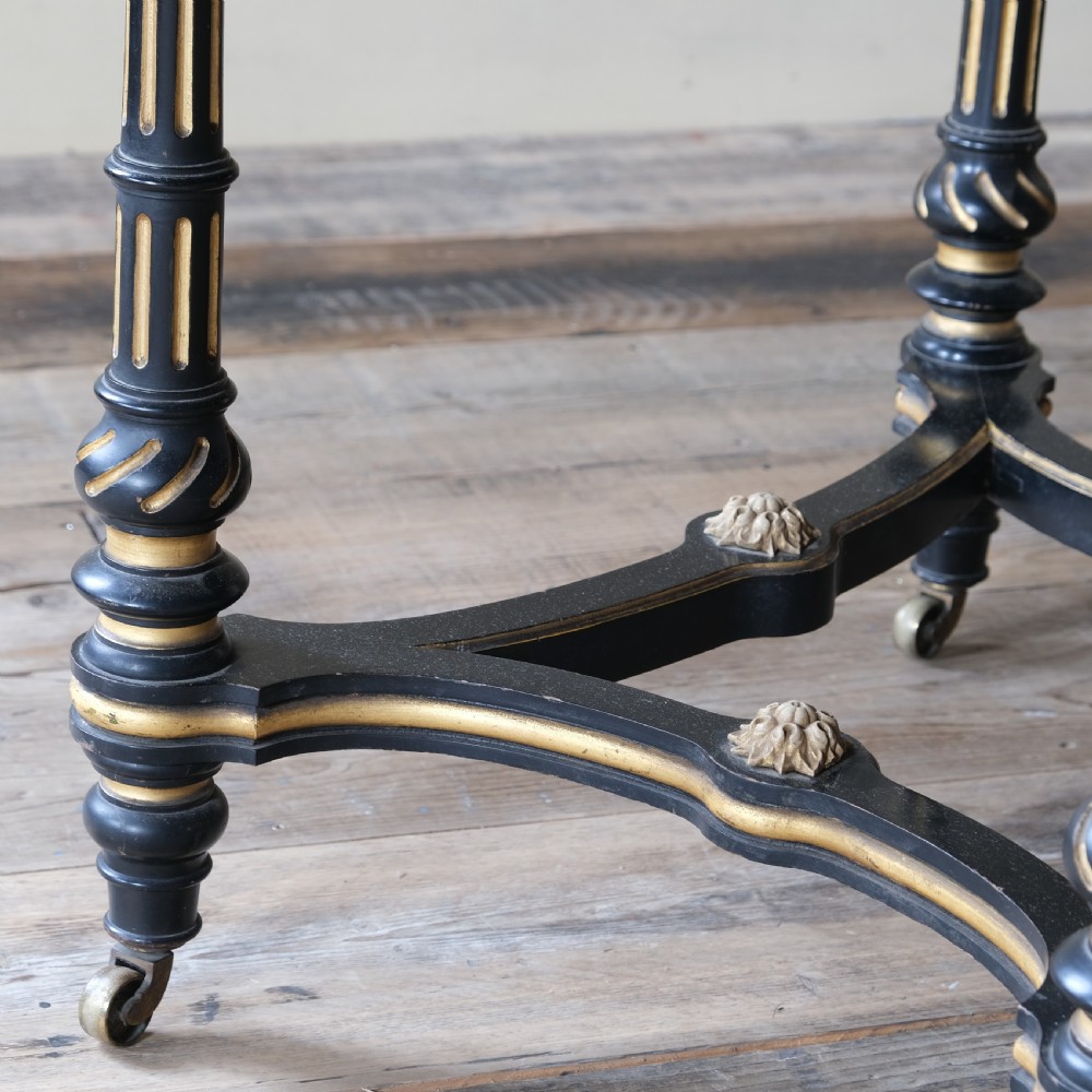 An Aesthetic Movement ebonised and parcel-gilt square table featuring fluted turned legs, a tassel fringe skirt, and brass castors. View XII