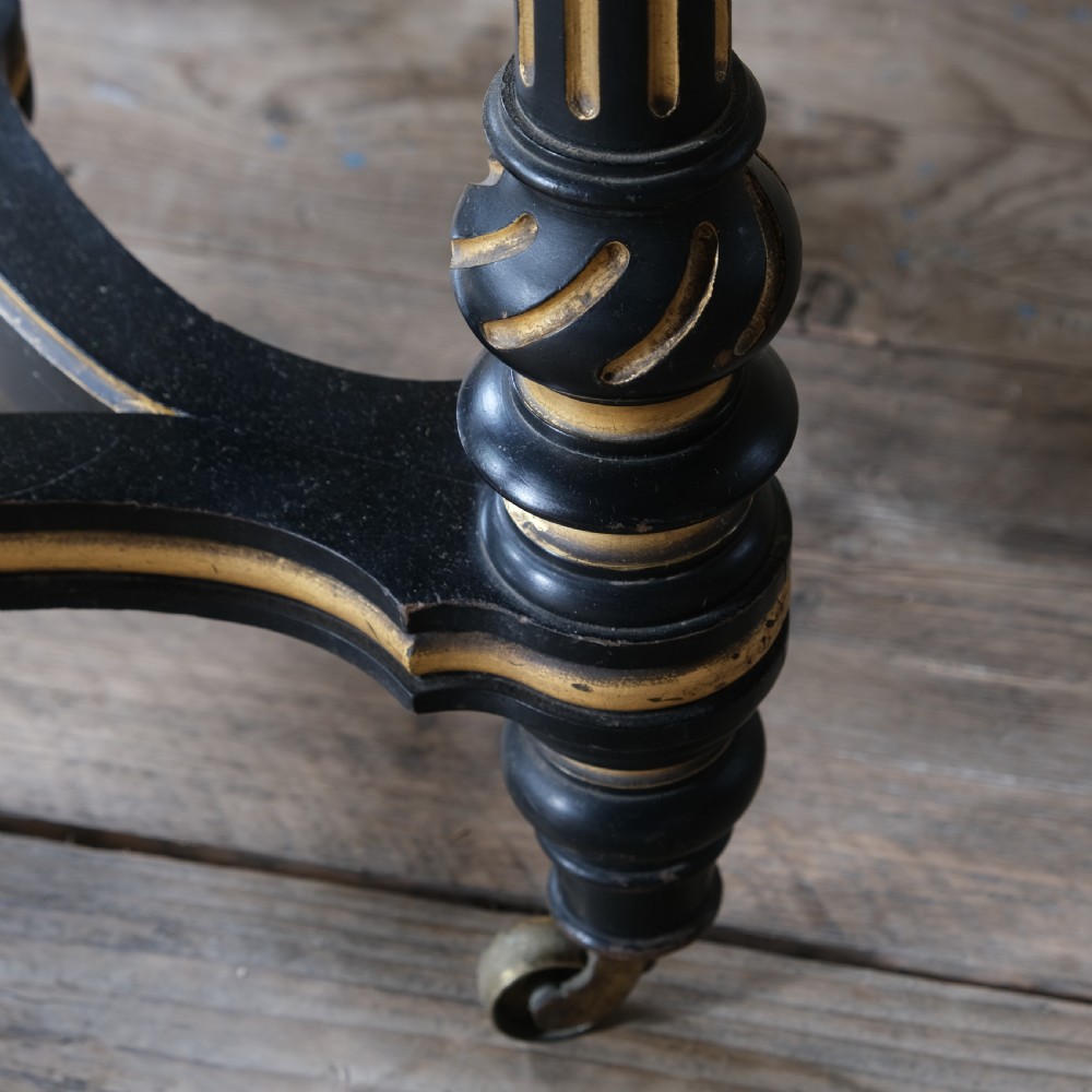 An Aesthetic Movement ebonised and parcel-gilt square table featuring fluted turned legs, a tassel fringe skirt, and brass castors. View XVI