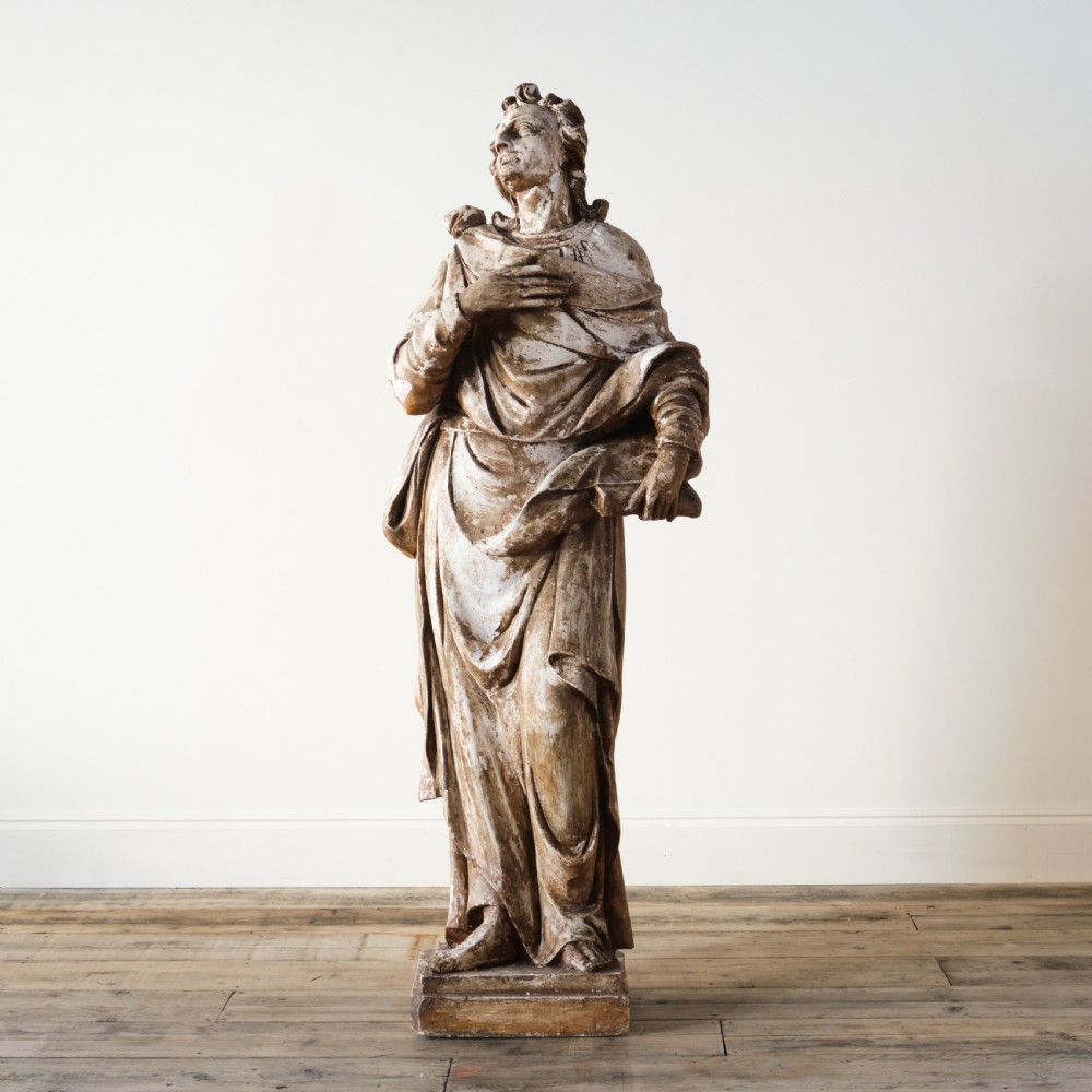 A large freestanding ecclesiastical plaster statue of a saint wearing draped robes, resting on a square pedestal with a distressed brown patinated surface. View II