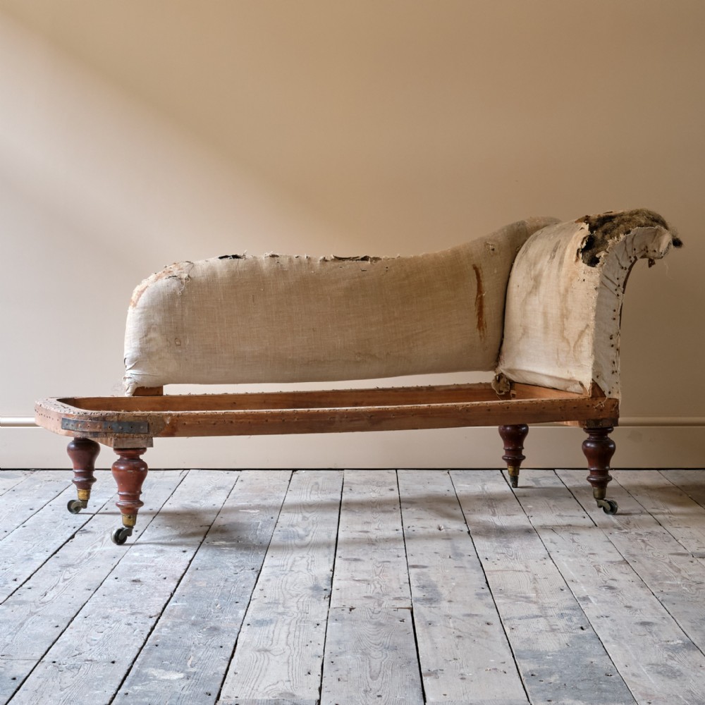 A mid-19th-century Victorian chaise longue frame featuring calico upholstery lining, turned mahogany legs, and brass castors.