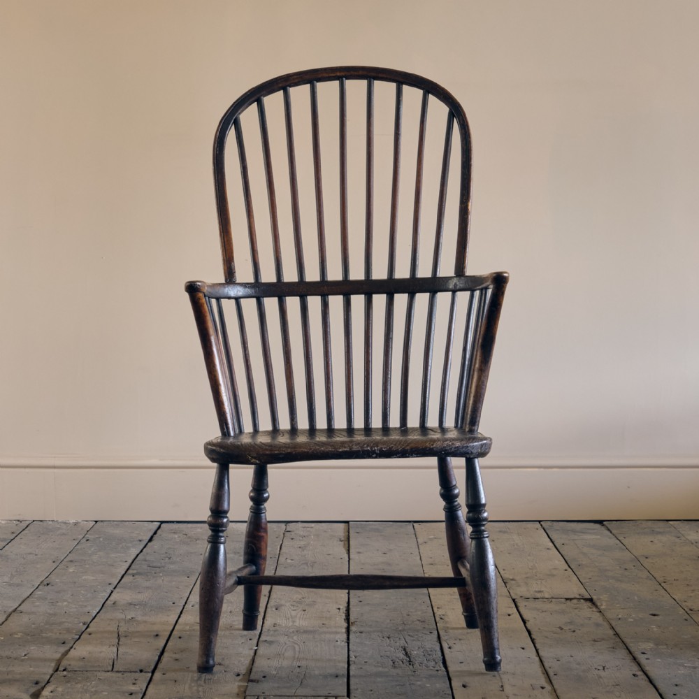 An early 19th-century dark wood hoop back Windsor armchair with vertical spindles, a contoured saddle seat, and turned legs with stretchers.
