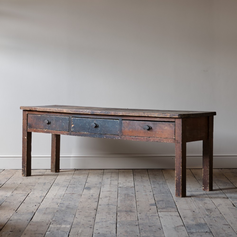 An antique dark pine dresser base featuring three inline drawers and straight square legs with a distressed finish.