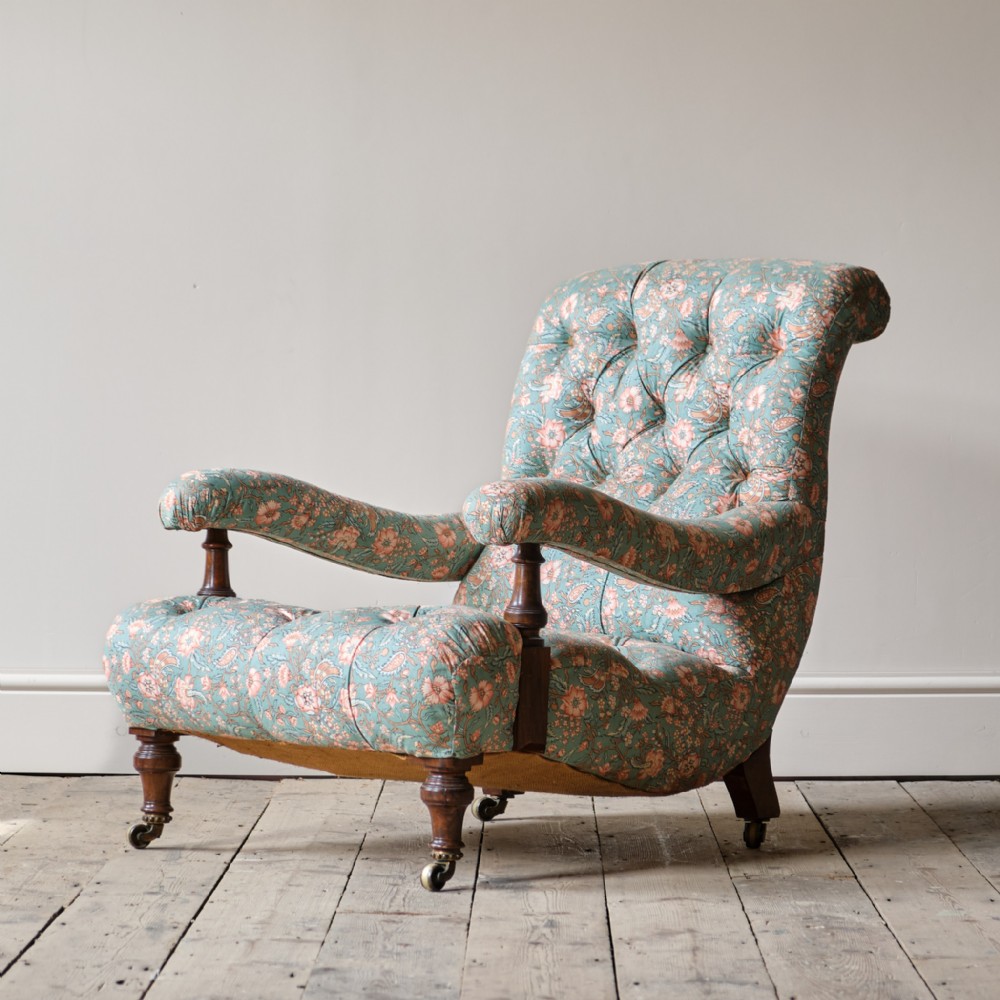 A Victorian open armchair featuring deep buttoned teal floral upholstery, turned mahogany arm supports, and brass castors.