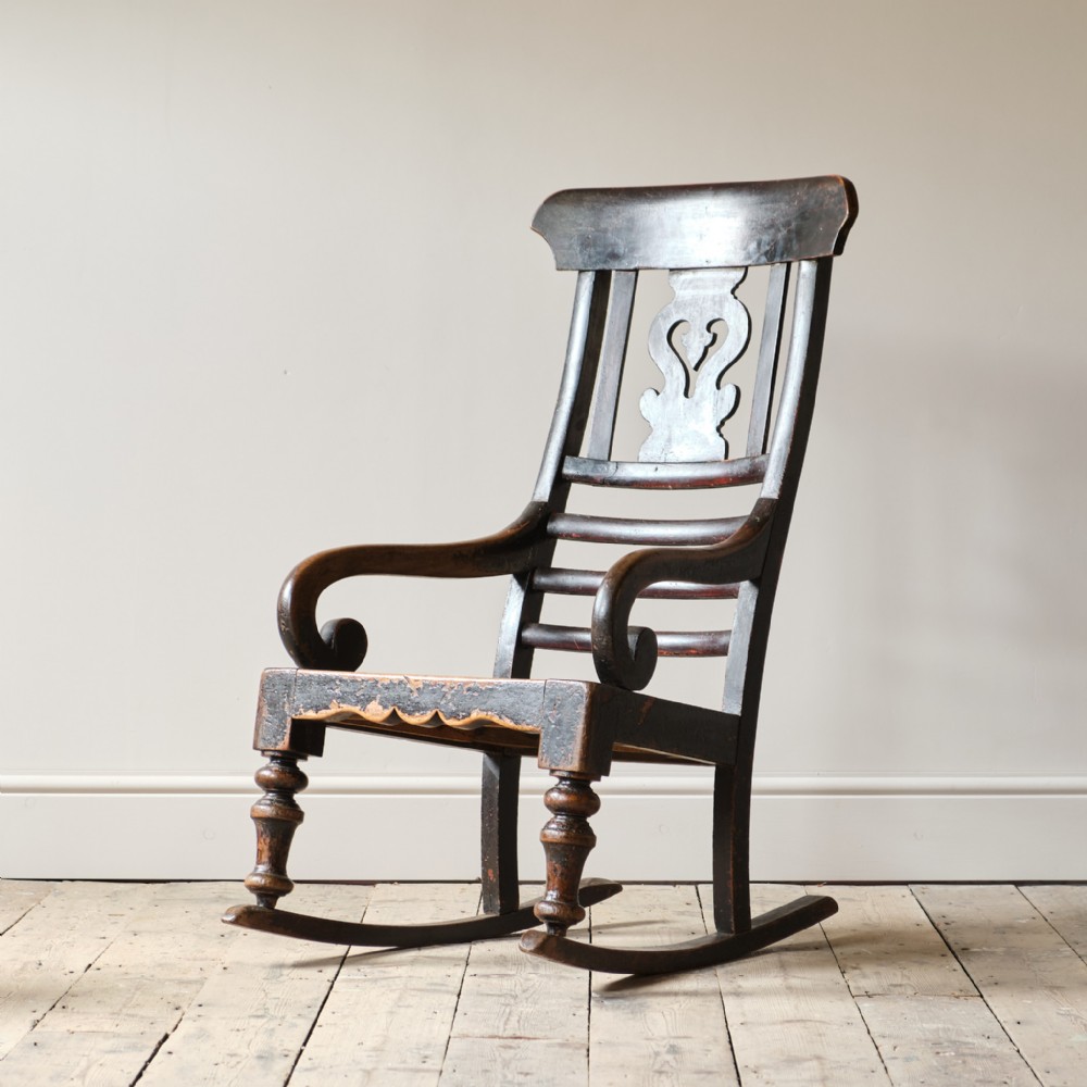 A dark-stained 19th-century wooden rocking chair featuring a pierced heart splat back, scrolled armrests, and turned front legs mounted on curved runners.