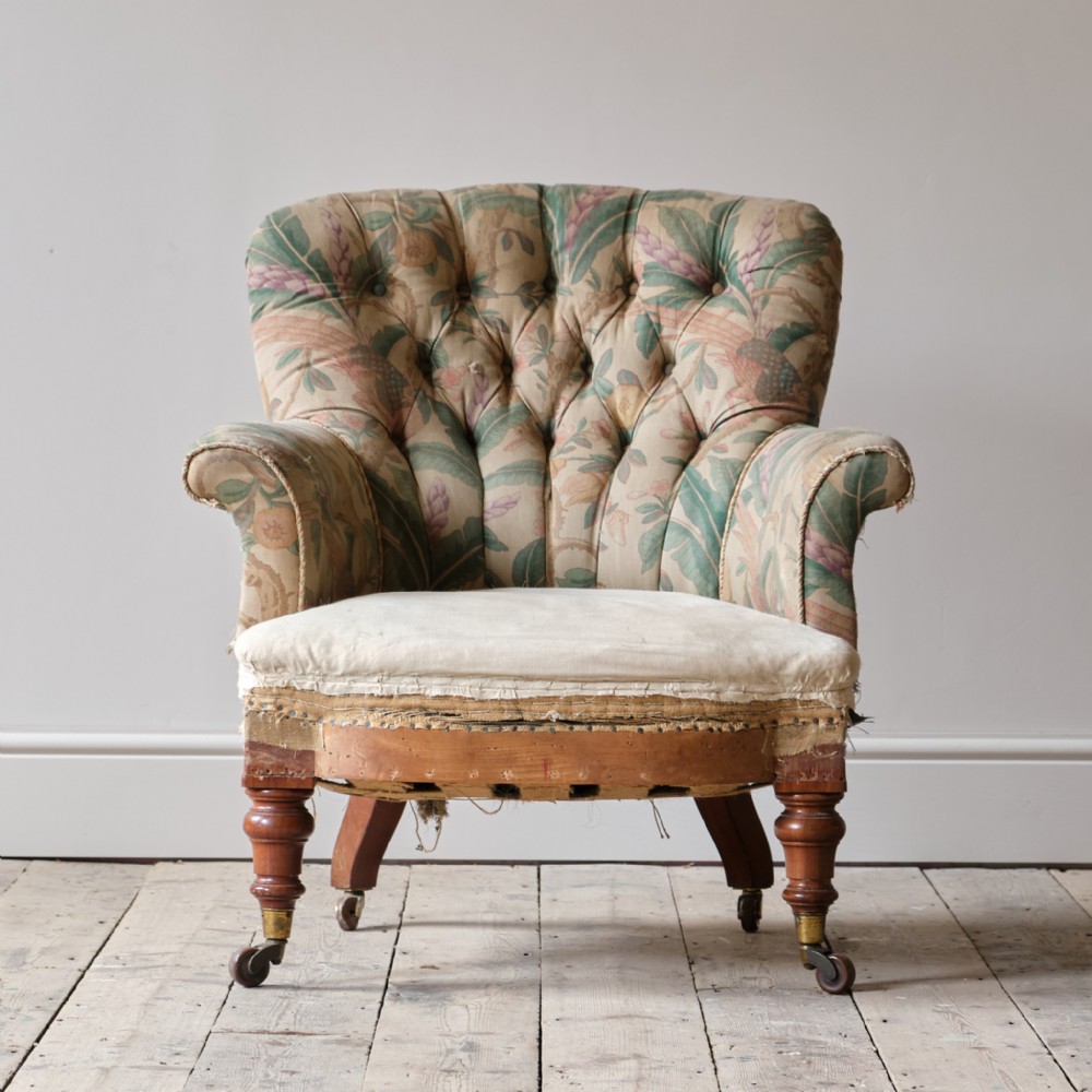 A nineteenth-century country house armchair featuring deep buttoned floral upholstery, turned front legs, and brass castors.