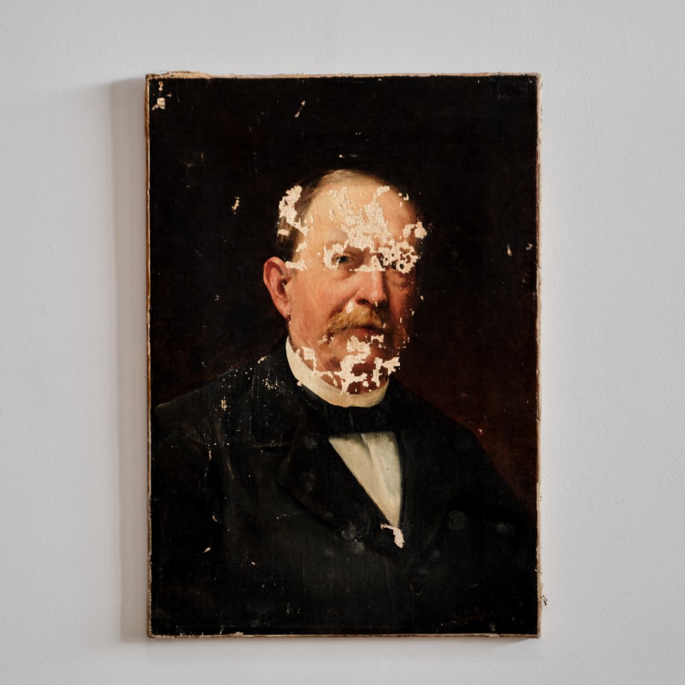 An unframed 19th-century oil portrait of a gentleman with a moustache in dark formal attire, showing surface wear and paint loss across the face.