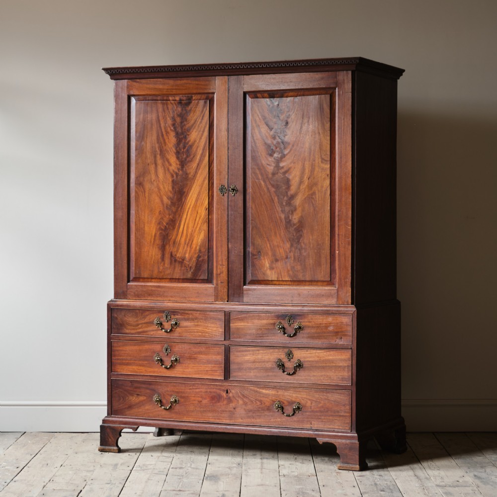 A George III mahogany linen press featuring a two-door upper cabinet with flame mahogany panels above a base of drawers on bracket feet.