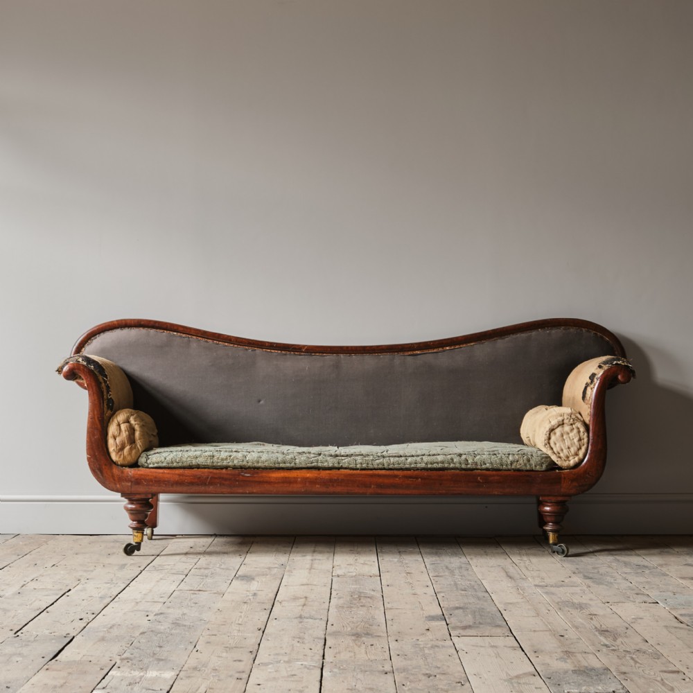 A 19th-century early Victorian mahogany sofa featuring scroll arms, patterned green fabric backrest, grey cushion, and turned legs on brass castors.