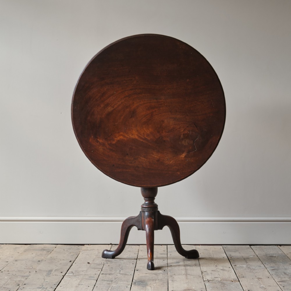 A George III dark mahogany circular tilt-top tripod table positioned vertically above a turned central column and three cabriole legs.