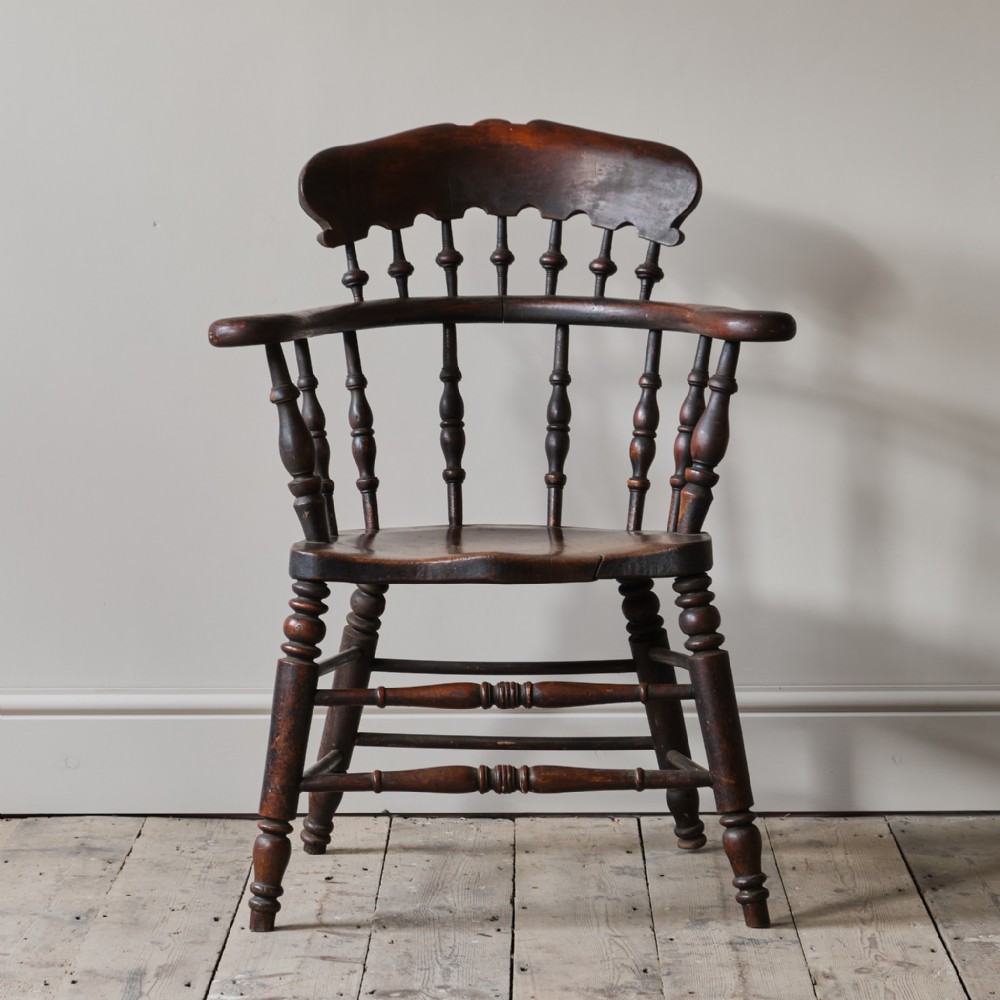 A 19th-century dark wood Smokers Bow Windsor armchair with a shaped crest rail, turned spindles, contoured seat, and turned legs with stretchers.