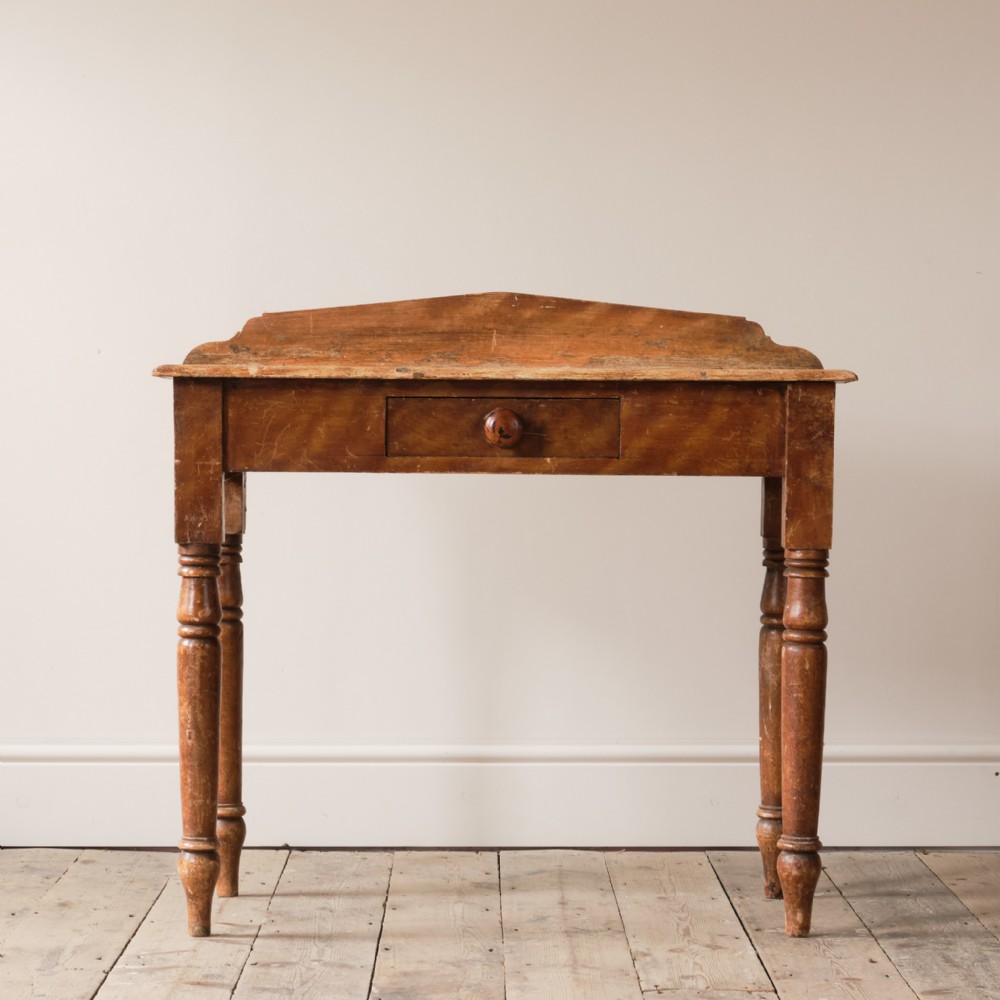 A 19th-century painted pine console table with turned legs, a single central drawer, and a low shaped back gallery top.