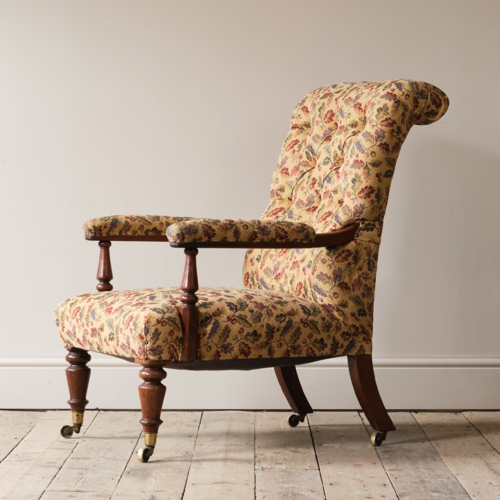 A mid 19th-century Victorian open armchair featuring floral pattern upholstery, button-tufted backrest, open padded arms, turned mahogany front legs, and brass castors.