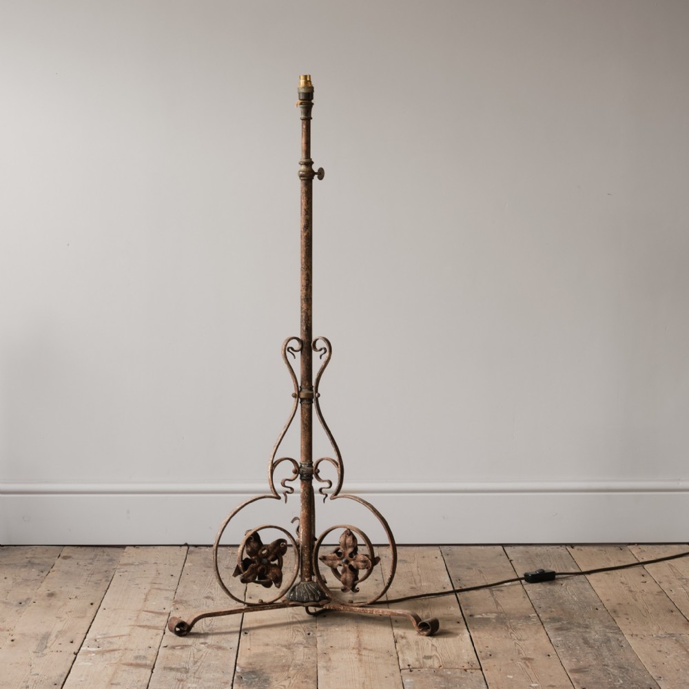 An adjustable wrought iron standard lamp featuring scrolled foliate metalwork and a tripod base.