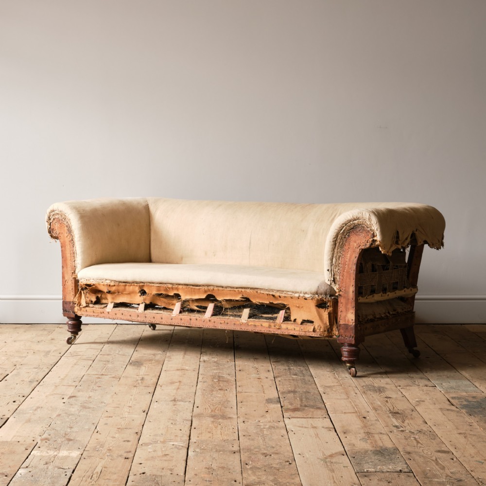 A late nineteenth-century Victorian Chesterfield sofa in a deconstructed calico state, featuring rolled arms, exposed webbing, and turned mahogany legs on brass castors.