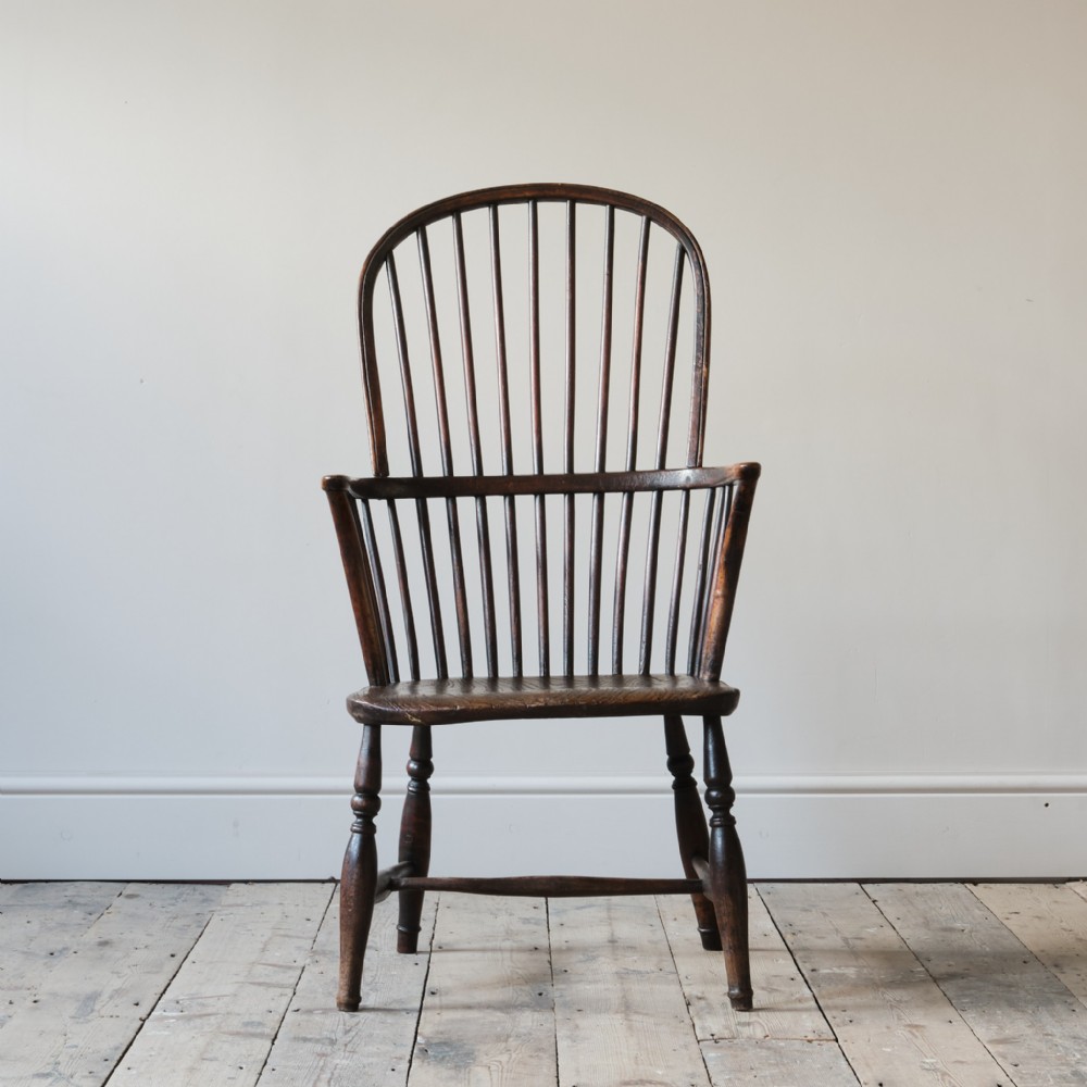 An early 19th-century dark wood hoop back Windsor armchair with vertical spindles, a contoured saddle seat, and turned legs with stretchers.