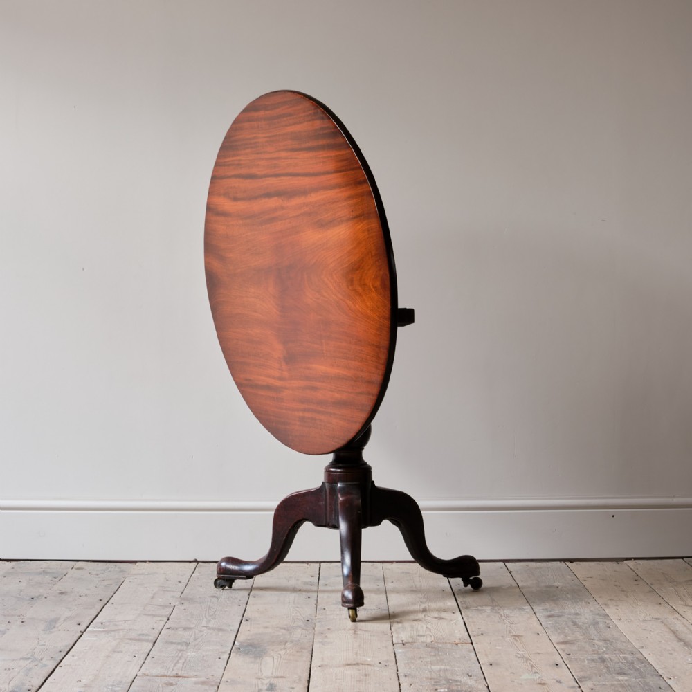 An 18th-century Georgian mahogany tilt-top table positioned vertically on a turned pedestal with tripod cabriole legs and brass castors.