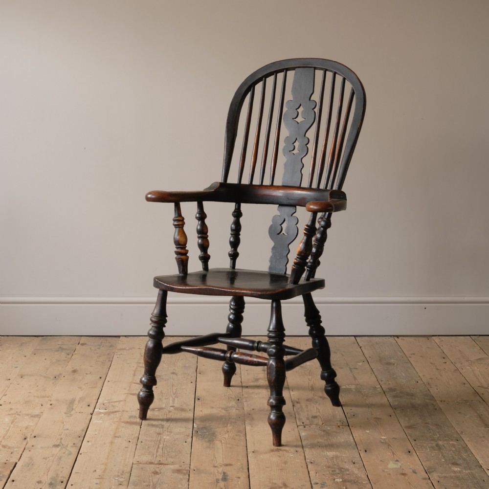 A 19th-century broad arm Windsor armchair crafted from ash and elm with a dark patinated finish, hoop back, turned legs, and a central pierced splat.