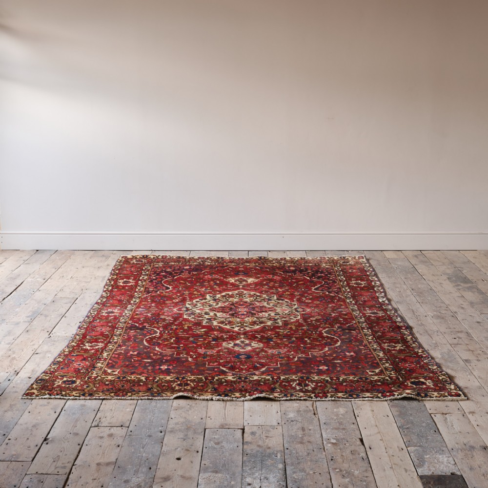 A large hand-knotted red Persian wool rug with a detailed ivory central medallion and elaborate floral borders laid flat on floorboards.