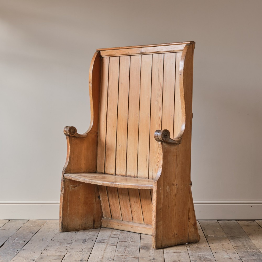 A 19th-century pine and elm high-backed settle featuring scrolled armrests and vertical plank construction.