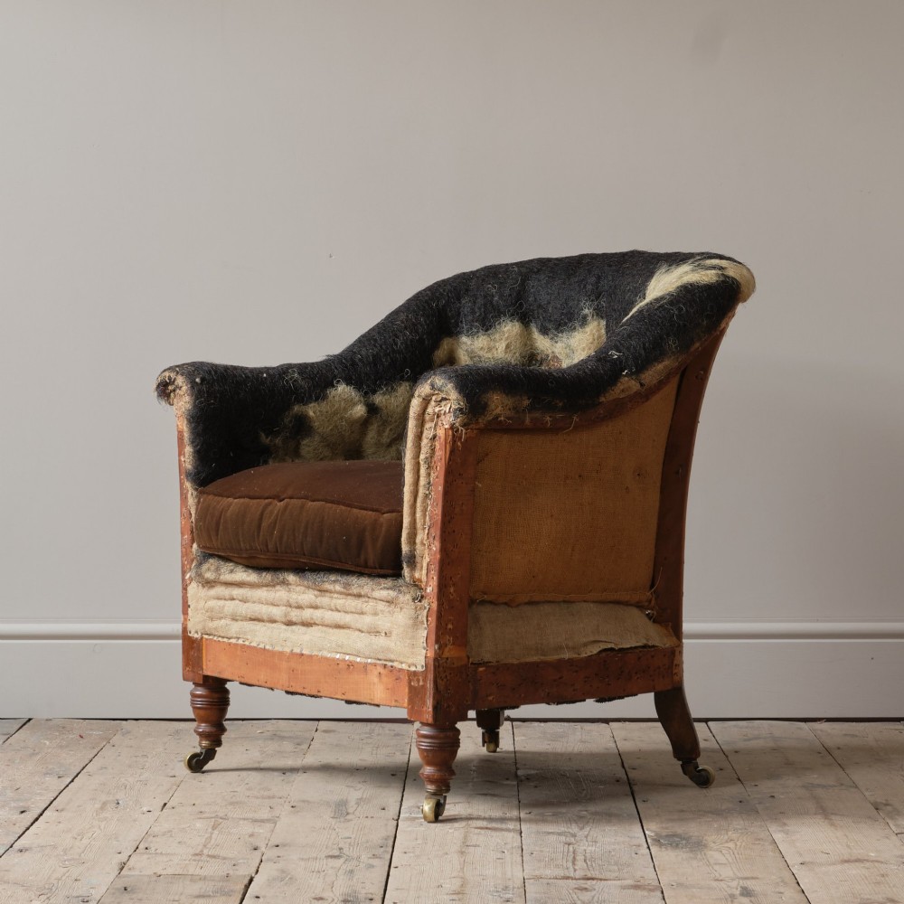 A 19th-century Howard and Sons Pickwell tub armchair showing exposed original hessian, horsehair filling, a brown velvet seat cushion, turned wooden legs, and brass castors. View II