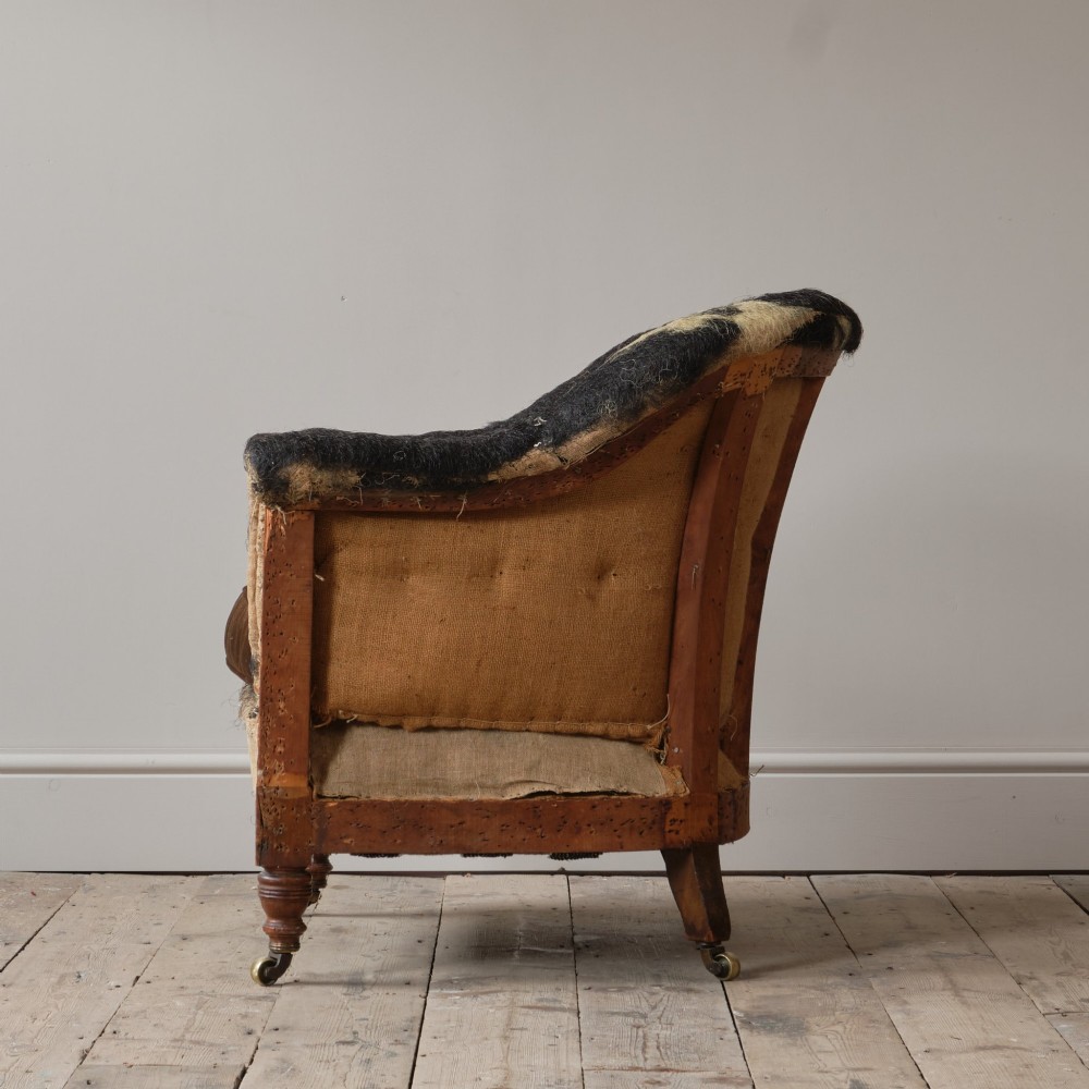 A 19th-century Howard and Sons Pickwell tub armchair showing exposed original hessian, horsehair filling, a brown velvet seat cushion, turned wooden legs, and brass castors. View III