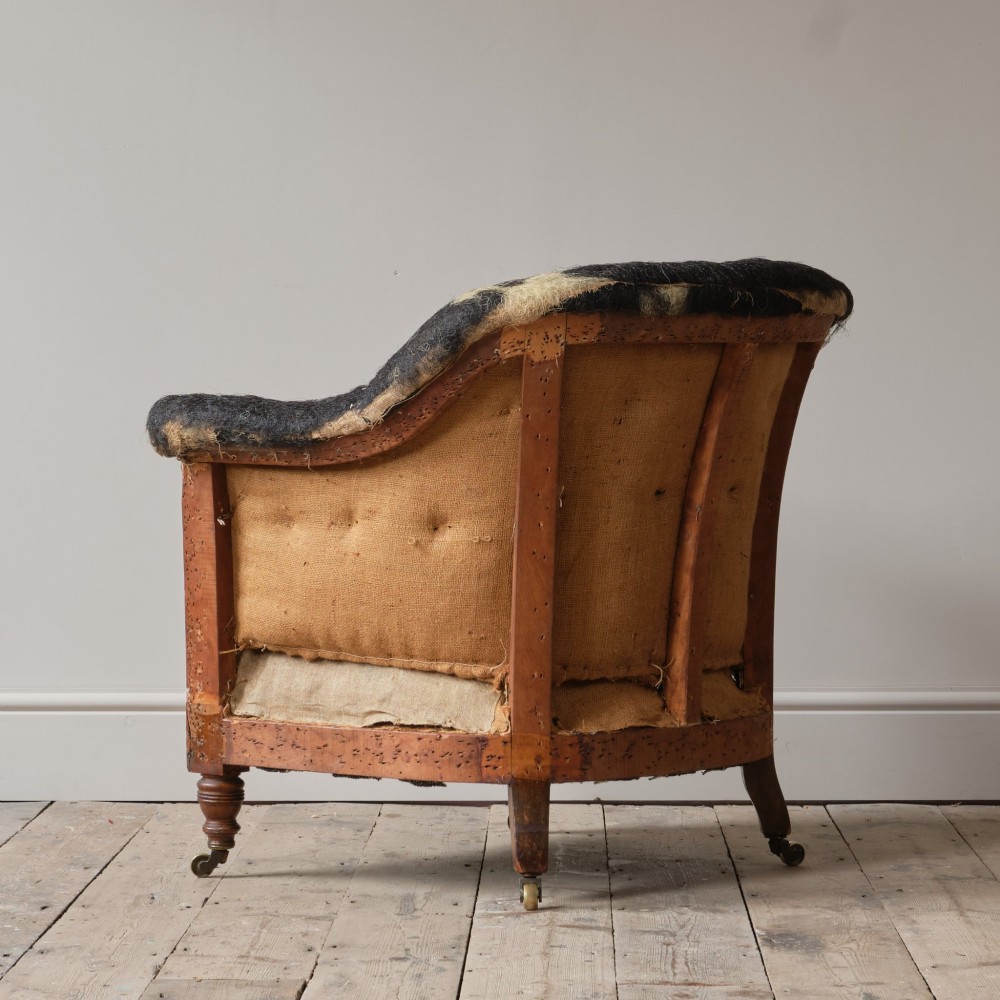 A 19th-century Howard and Sons Pickwell tub armchair showing exposed original hessian, horsehair filling, a brown velvet seat cushion, turned wooden legs, and brass castors. View IV