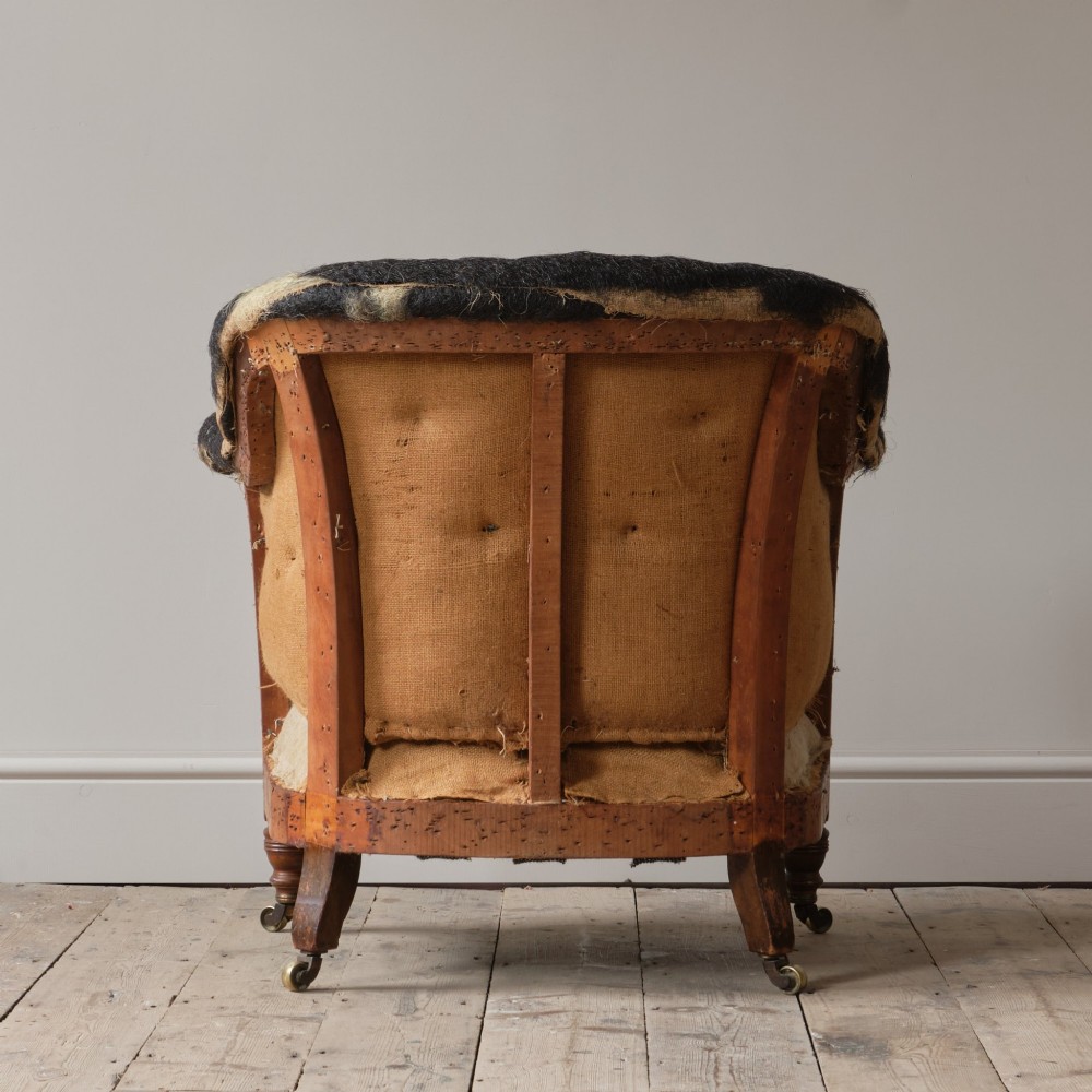 A 19th-century Howard and Sons Pickwell tub armchair showing exposed original hessian, horsehair filling, a brown velvet seat cushion, turned wooden legs, and brass castors. View V