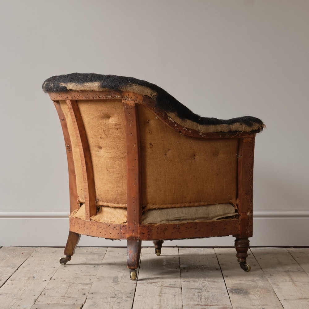 A 19th-century Howard and Sons Pickwell tub armchair showing exposed original hessian, horsehair filling, a brown velvet seat cushion, turned wooden legs, and brass castors. View VI