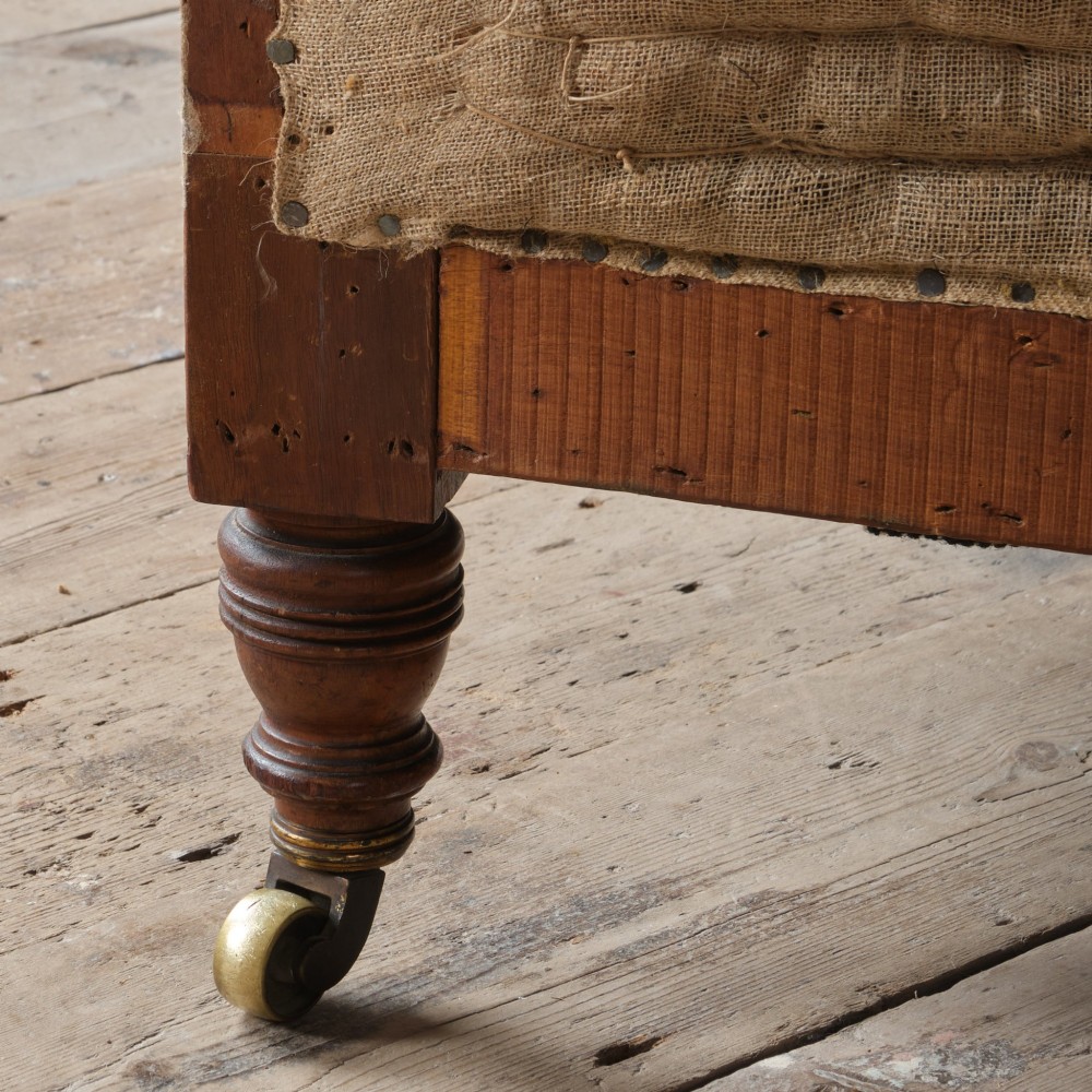 A 19th-century Howard and Sons Pickwell tub armchair showing exposed original hessian, horsehair filling, a brown velvet seat cushion, turned wooden legs, and brass castors. View XI