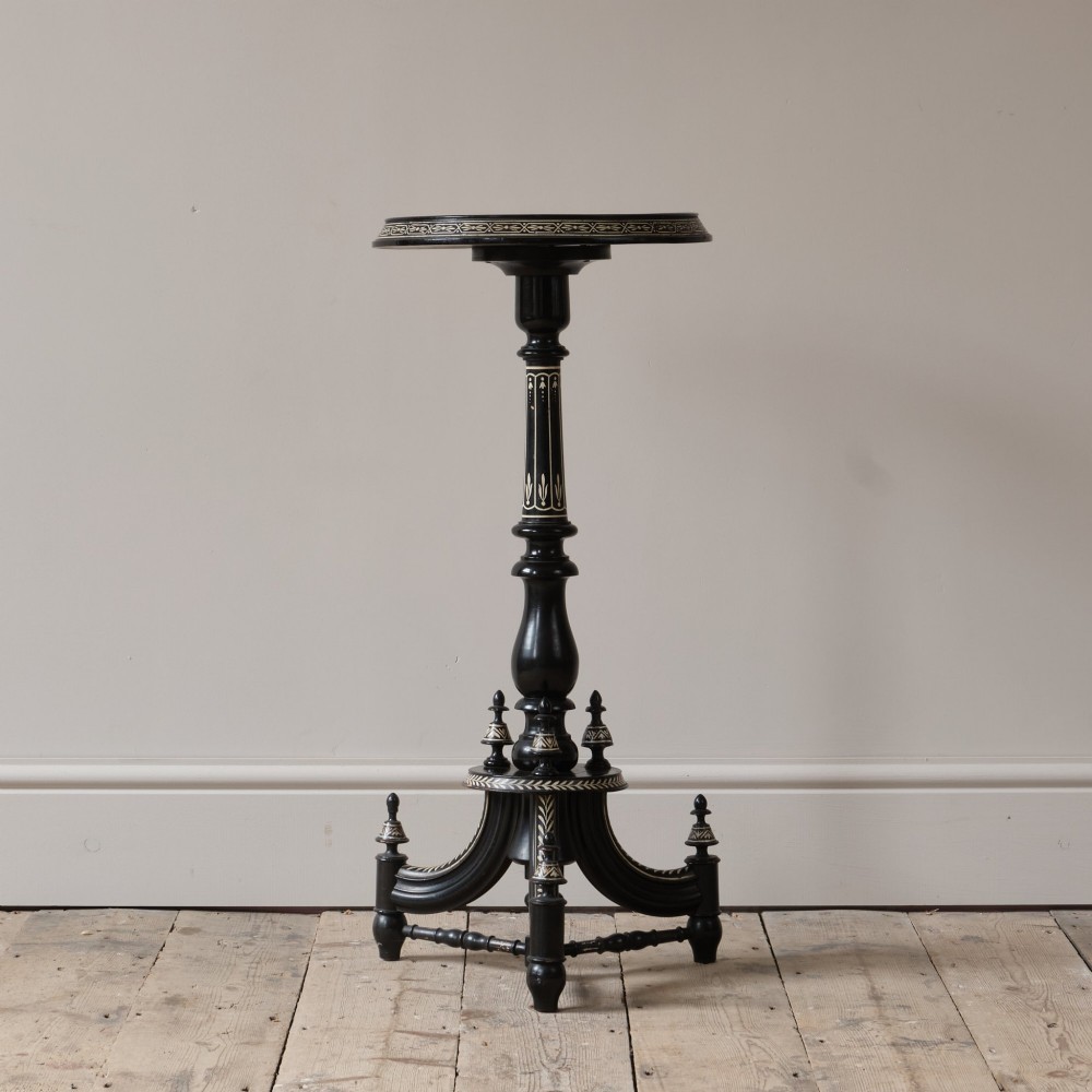 A 19th-century Aesthetic Movement ebonised tripod side table featuring a circular top, turned central column, light-coloured decorative inlay, and finial details.