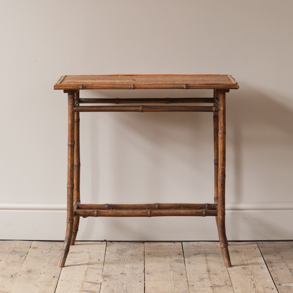 An early 20th-century bamboo side table featuring a rectangular woven cane top, bamboo legs, and lower cross stretchers.