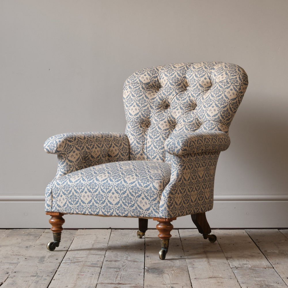 A mid-19th century Victorian upholstered armchair featuring blue and cream patterned fabric, deep button-tufted backrest, turned wooden front legs, and brass castors. View II