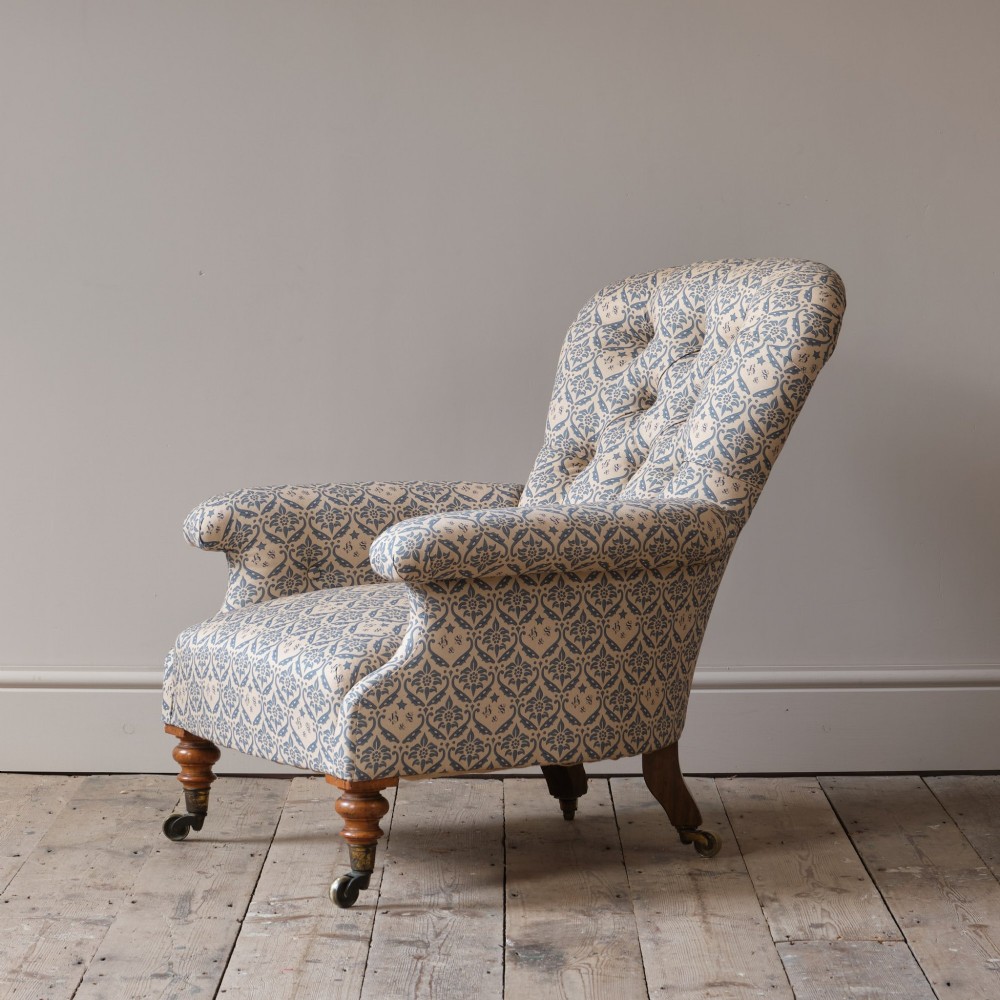 A mid-19th century Victorian upholstered armchair featuring blue and cream patterned fabric, deep button-tufted backrest, turned wooden front legs, and brass castors. View III