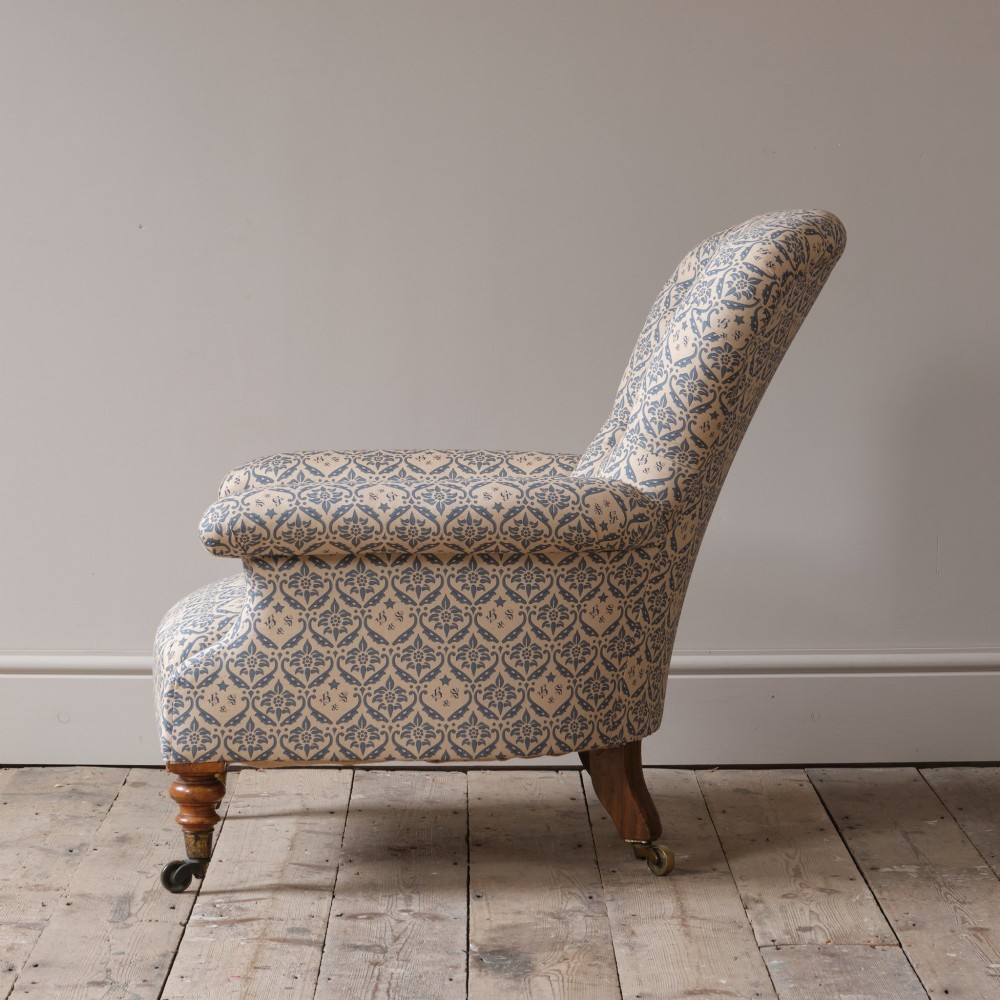 A mid-19th century Victorian upholstered armchair featuring blue and cream patterned fabric, deep button-tufted backrest, turned wooden front legs, and brass castors. View IV
