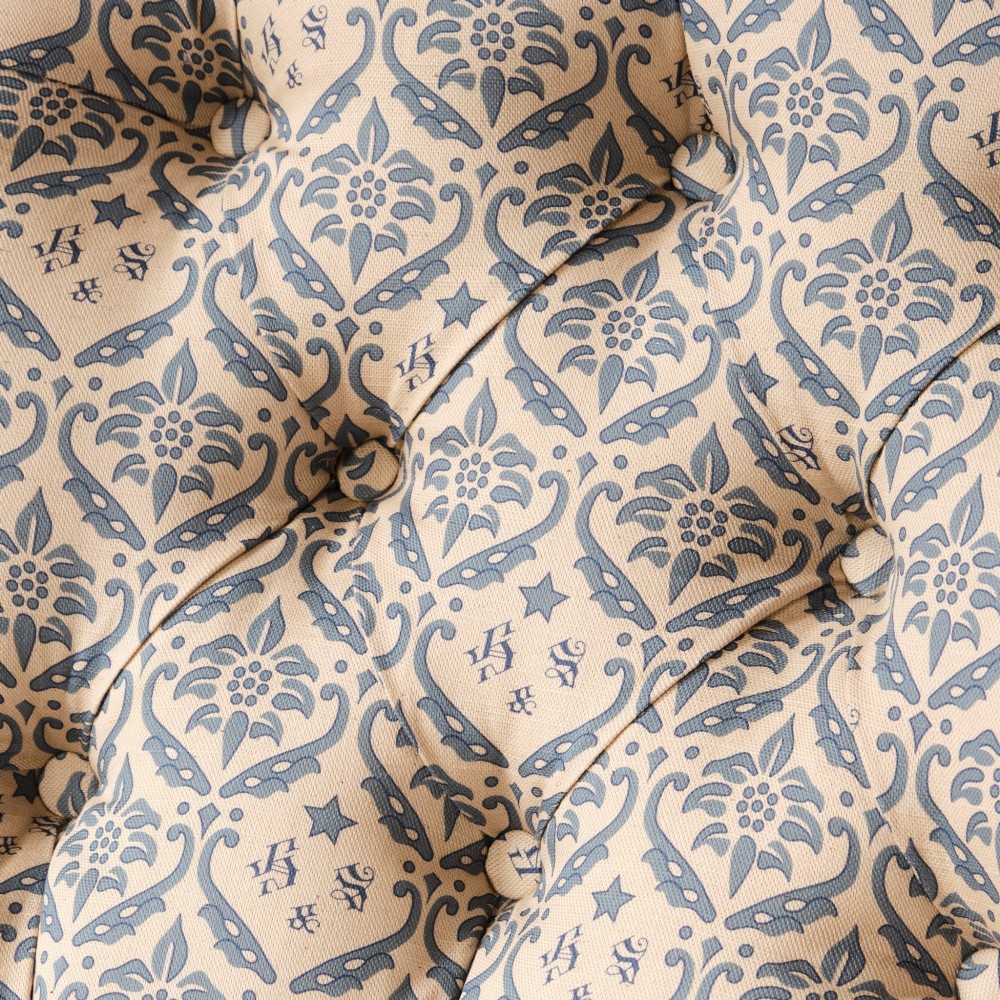 A mid-19th century Victorian upholstered armchair featuring blue and cream patterned fabric, deep button-tufted backrest, turned wooden front legs, and brass castors. View V