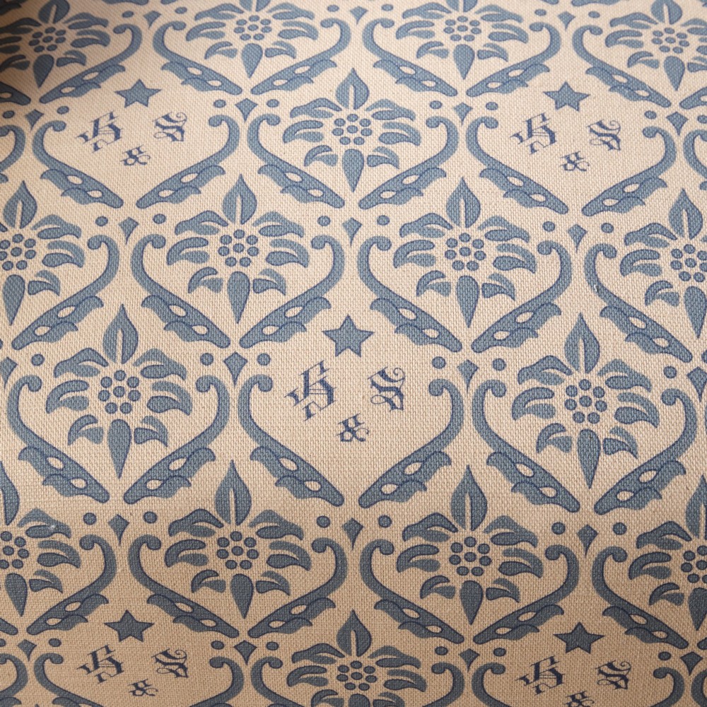 A mid-19th century Victorian upholstered armchair featuring blue and cream patterned fabric, deep button-tufted backrest, turned wooden front legs, and brass castors. View VI